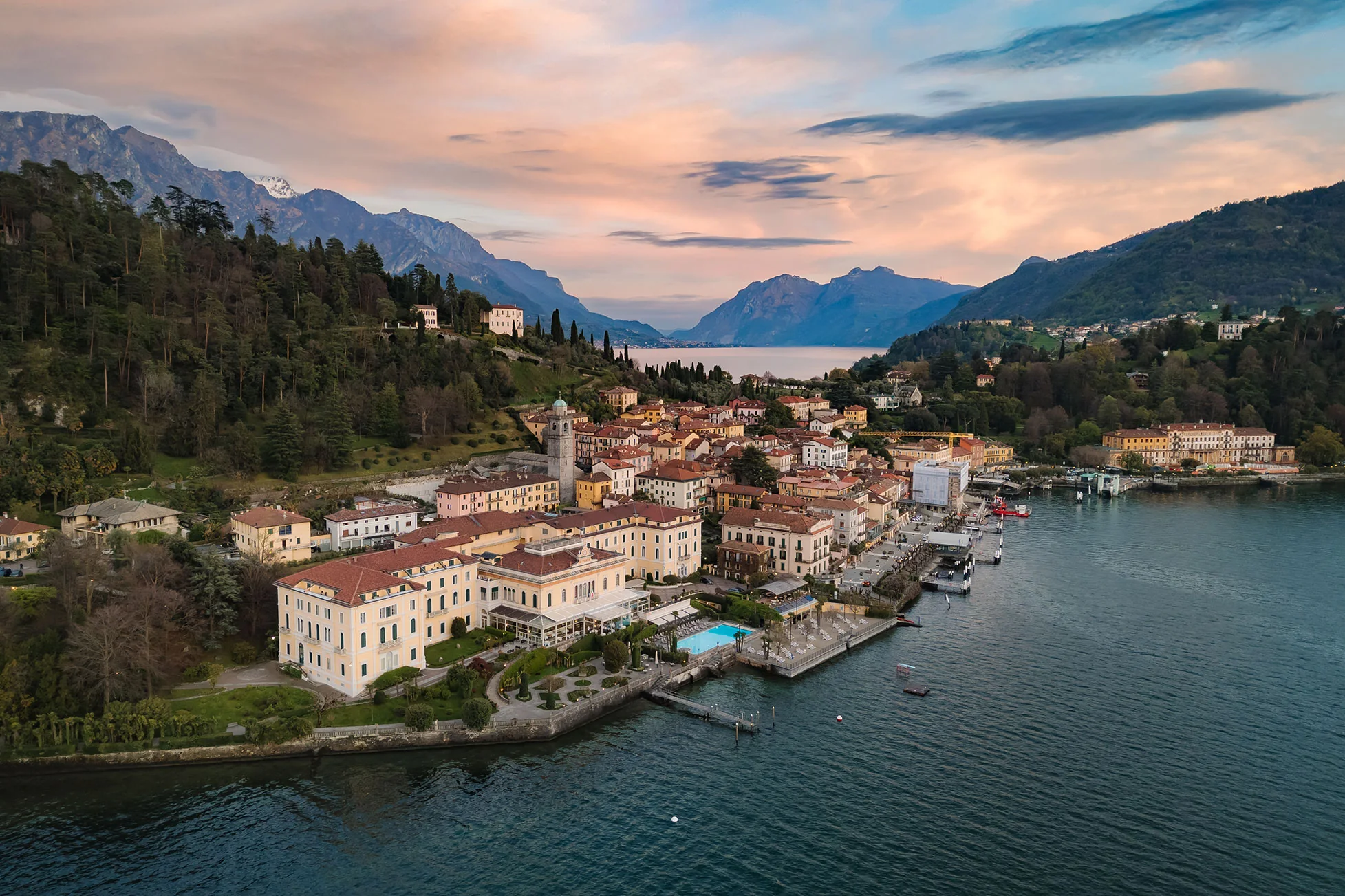 Grand Hotel Villa Serbelloni on the Bellagio waterfront, seen from above at dusk, with gardens and dock on Lake Como